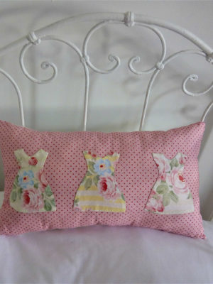 Petit coussin rectangulaire dimensions 26 X 45 cms Le fond du coussin est rose à petits pois Le coussin est agrémenté de 3 petites robes dans un tissu fleuri aux tons roses et jaunes, appliquées à petits points serrés La face arrière du coussin est blanche avec un petit coeur rose brodé main Matière du coussin 100 % coton Intérieur du coussin 100% polyester Conseil de lavage 30°