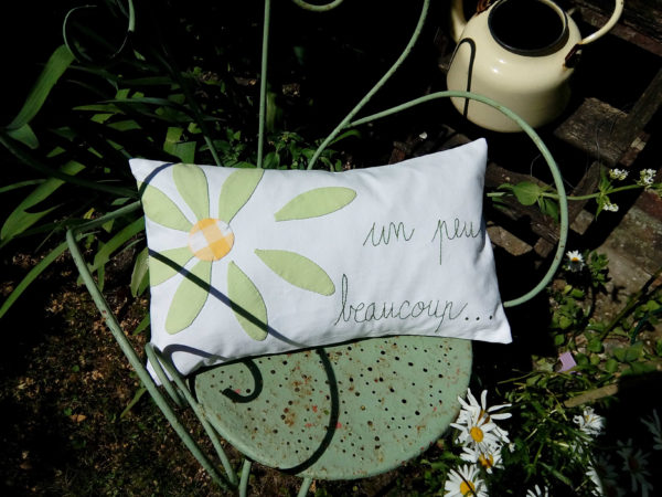 coussin rectangulaire en tissu recyclé, dimensions du coussin 30 cms par 50 cms, grosse marguerite verte appliquée sur un fond blanc, mot un peu beaucoup brodés main, coussin déhoussable finition portefeuille, intérieur 100% polyester